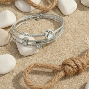 Silver bracelet with beads on a sandy surface with stones and rope