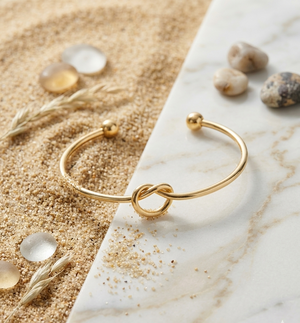 Gold bracelet on a marble surface with sand and stones in the background