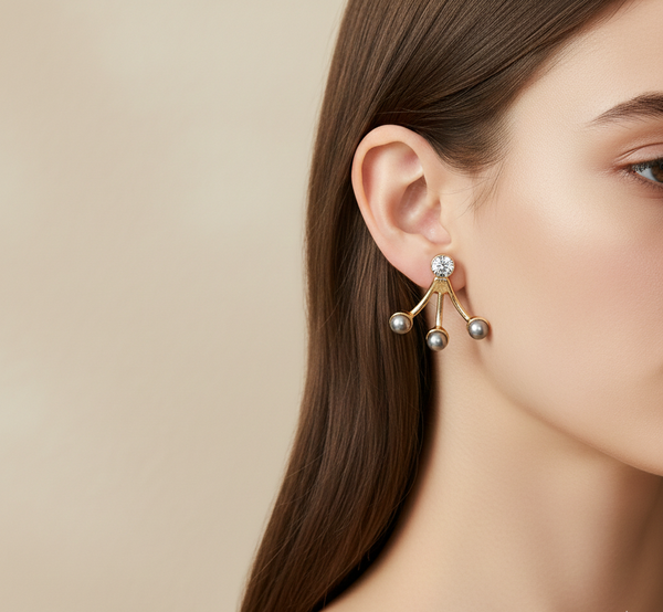 Close-up of a woman wearing a gold earring with three pearl-like stones on a beige background