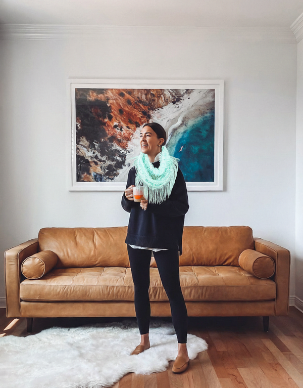 Woman standing in a living room with a brown leather sofa and abstract art on the wall.