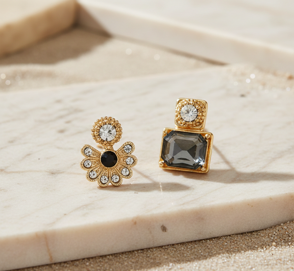 Two gold earrings with gemstones on a marble surface