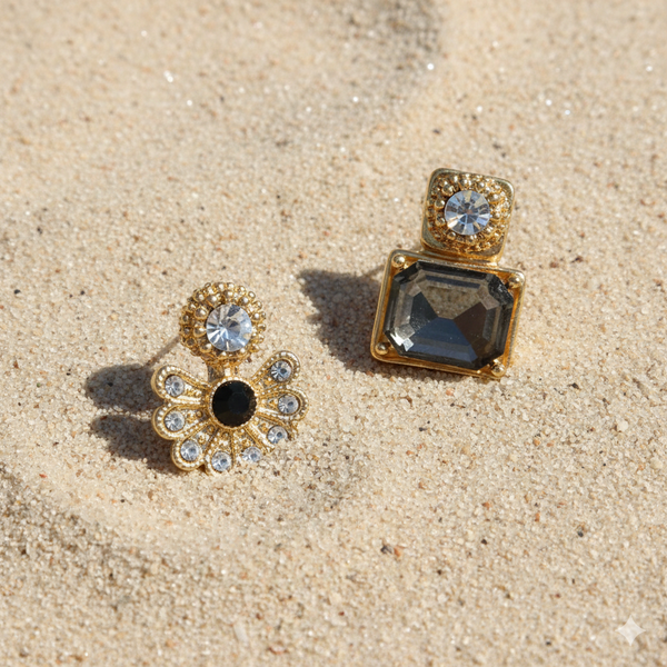 Two gold and crystal earrings on a sandy surface