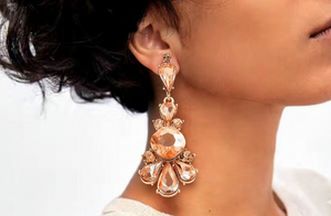 Close-up of a person wearing a rose gold earring with clear gemstones.