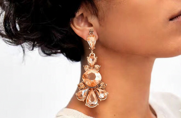 Close-up of a person wearing a rose gold earring with clear gemstones.