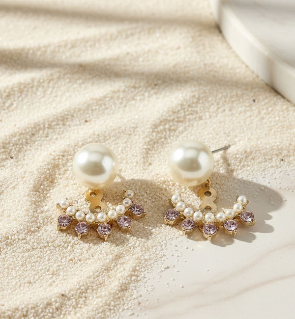 Pearl earrings with small purple stones on a sandy surface
