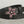 Load image into Gallery viewer, A black leather belt with a large, ornate silver-tone buckle featuring pink rhinestones, coiled on a light gray wooden surface.
