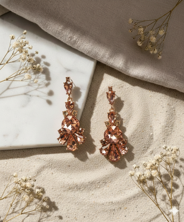 Rose gold earrings on a textured surface with dried flowers