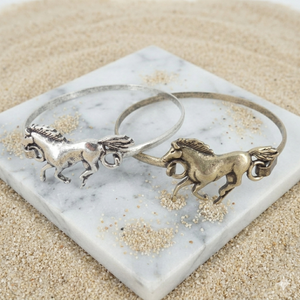 Two horse-themed bracelets on a marble coaster with sand around.