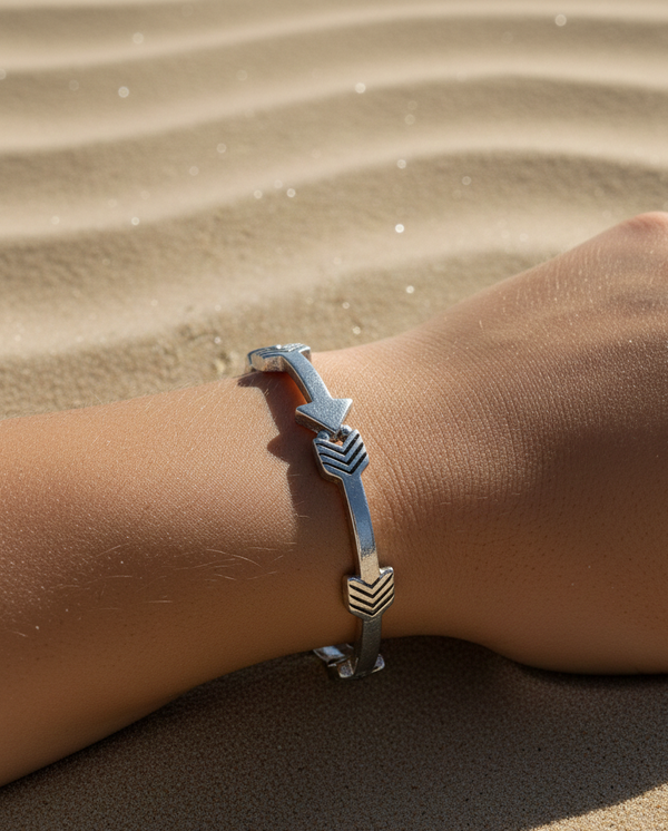 Silver bracelet with arrow design on a wrist against a sandy background
