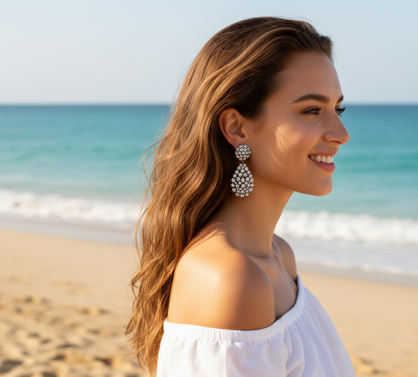 Woman wearing a white off-shoulder top and large earrings on a beach with ocean view