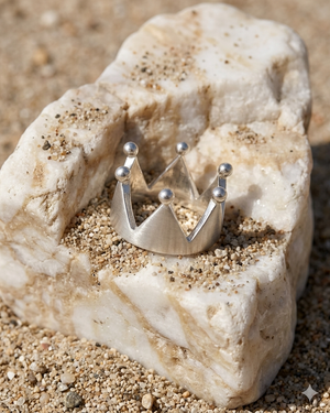 Silver crown-shaped ring on a piece of stone with sand around