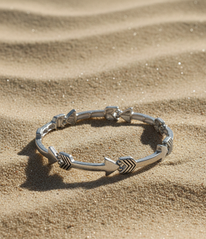 Silver bracelet with arrow designs on a sandy surface