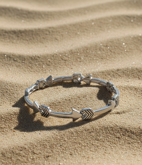 Silver bracelet with arrow designs on a sandy surface