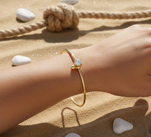 Gold bracelet with a diamond on a wrist against a sandy background