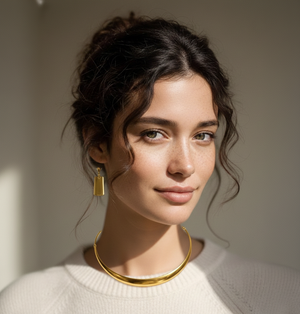Woman wearing gold hoop earrings and necklace against a neutral background