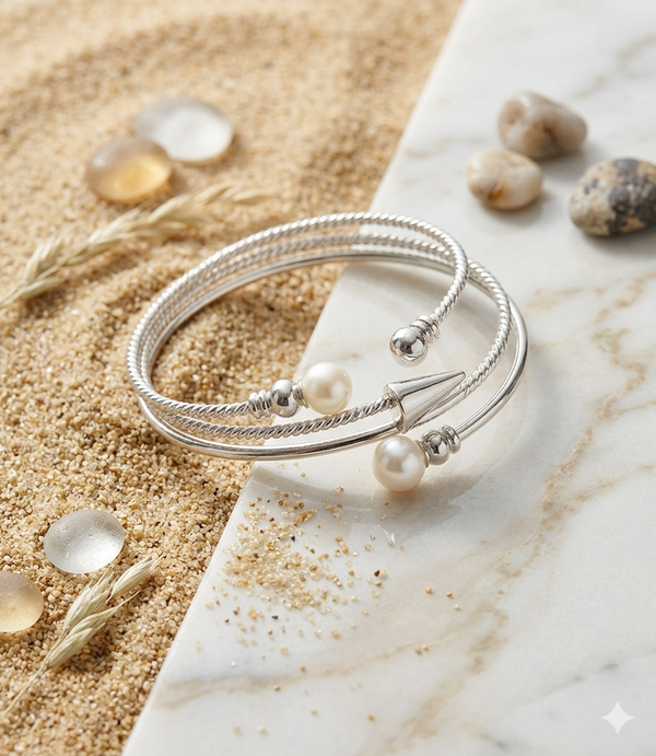 Silver bracelet with pearls on a marble surface with sand and shells in the background