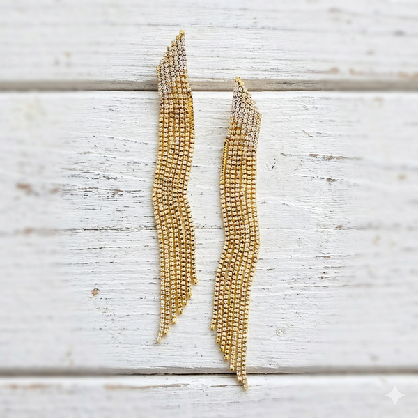 Gold beaded statement earrings on a light wooden surface