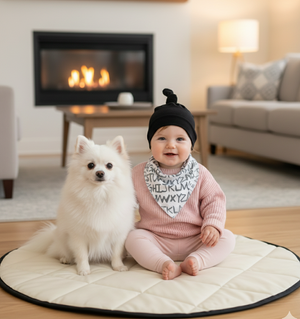 Baby sitting on a round mat with a white dog, in a cozy living room setting.