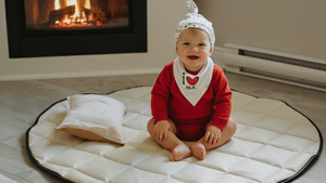 Baby sitting on a round mat in front of a fireplace
