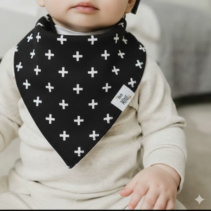 Baby wearing a black bib with white cross patterns, sitting on a couch.