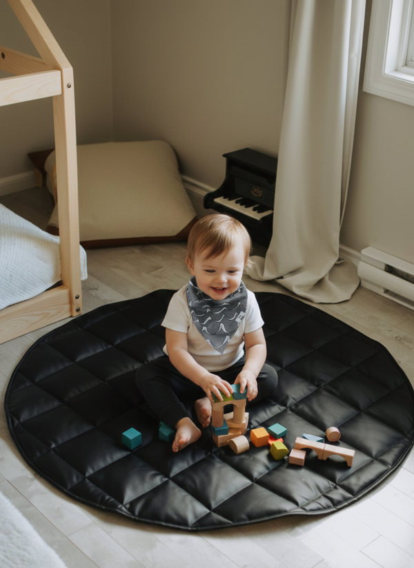 Child playing with building blocks on a black mat in a room with a piano and curtains.