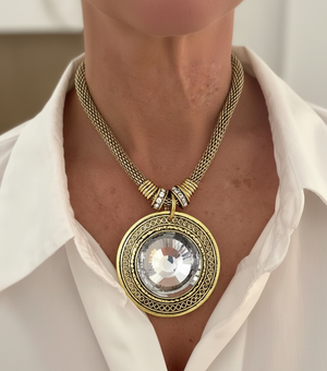 Gold necklace with a large pendant worn by a person in a white shirt.