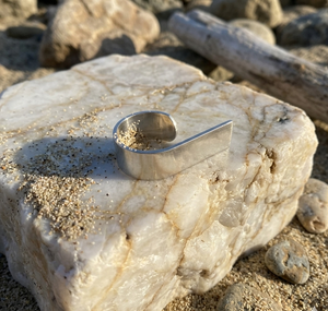 Metallic spoon on a textured stone surface with sand and driftwood in the background
