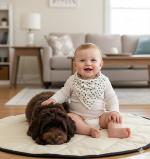 Baby sitting on a mat with a dog, both smiling, in a living room setting.