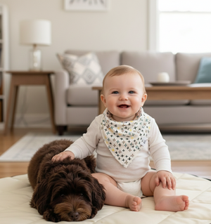 Baby sitting on a mat with a dog, both smiling, in a living room setting.
