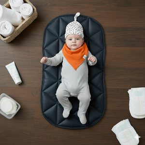 Baby lying on a dark mat with diaper changing supplies on a wooden surface