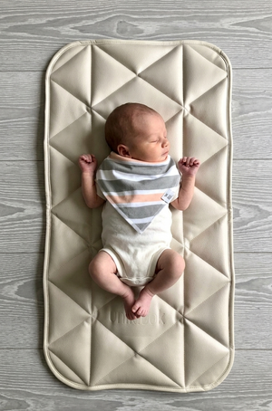 Newborn baby lying on a quilted mat with a wooden floor background